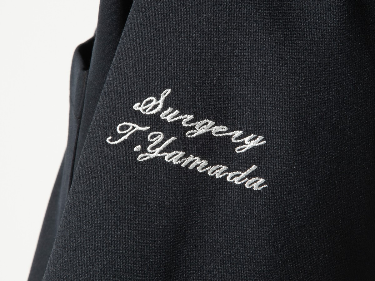 スクラブの袖に入れたネーム刺繍の例。診療科名「Surgery」と氏名「T.Yamada」の2行を筆記体で刺繍