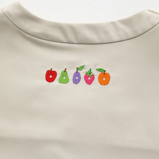 人気の絵本『はらぺこあおむし』と医療ウェアブランド「クラシコ」がコラボレーションしたスクラブ白衣(アイボリー：ベージュ色)のトップス背面のあおむしが食べた果物の刺繍